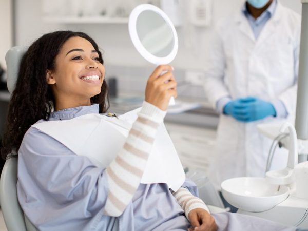 Happy,Black,Female,Patient,Looking,At,Mirror,After,Dental,Treatment